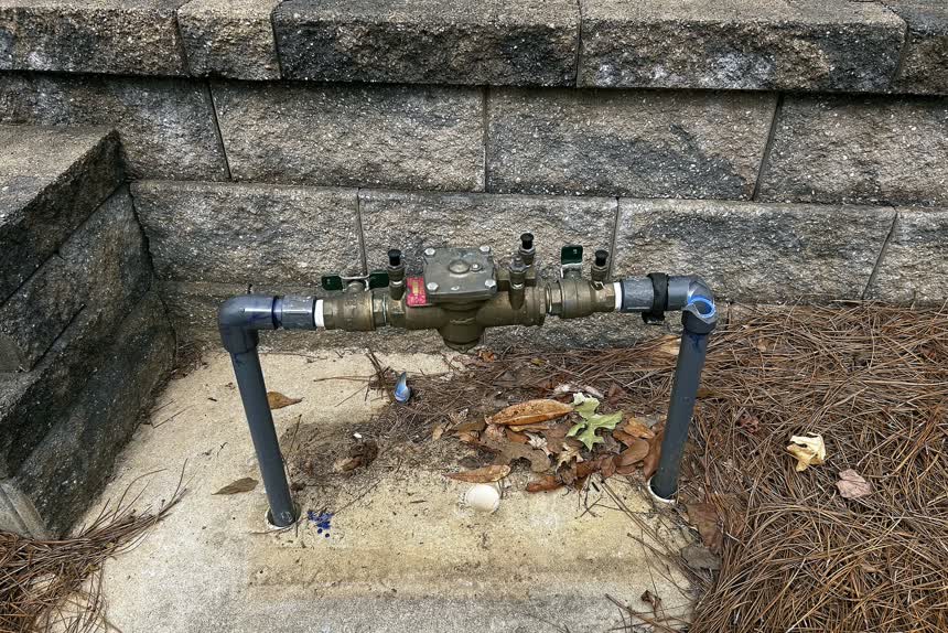 A backflow preventer beside a stone wall