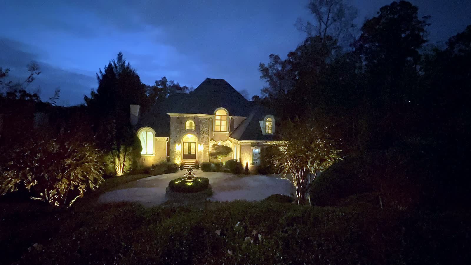 An estate facade and fountain lit at dusk